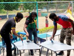 Member of Parliament for St Catherine East Central (centre) helps to paint desks at the Gregory Park Basic School.