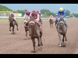 SHE’S A MANEATER (centre), ridden by Anthony Thomas, gallops by BIGDADDYKOOL to win the 39th running of the Burger King Superstakes at Caymanas Park on Saturday, November 11, 2017.