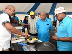Tourism Minister Ed Bartlett (right) gets a demonstration featuring plantains at the Denbigh Agricultural, Industrial and Food Show on Sunday, August 4. Jamaica Agricultural Society President Lenworth Fulton (second right) looks on.