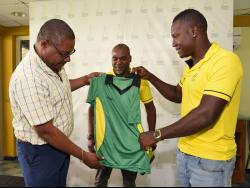 Courtney Francis (left), CEO of the Jamaica Cricket Association, hands over the Jamaica Scorpions 2019-20 kit to captain Rovman Powell (right) as coach André Coley looks on during a press conference at Sabina Park yesterday.