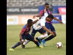 Jamaica College’s Isaac Scott (centre) weaves his way through Steven McQueen (left) and Rusean McFarquhar of St Andrew Technical High School during the Manning Cup final last Saturday.