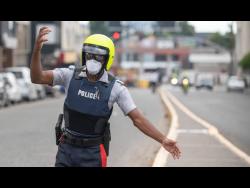 A member of the Jamaica Constabulary Force directs traffic in New Kingston while wearing a mask as a  preventative measure against COVID-19.