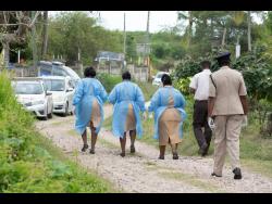 Ministry of Health and Wellness workers and police personnel at the residence of the 79-year-old male patient who was Jamaica’s first COVID-19 death.