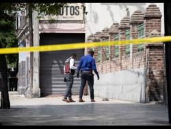 Credit: Gladstone Taylor Members of the Jamaica Constabulary Force examine the crime scene where an alleged thief was shot dead on Monday on East Parade in the vicinity of the Coke Memorial Methodist Church.