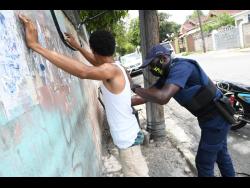 A member of the security forces searches a man along  Arnold Road in Kingston yesterday.