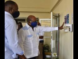 Minister of Tourism Edmund Bartlett (right) adheres to the protocols of a temperature check and hand sanitisation with automated equipment, ahead of entering the reception area of the Golf View Hotel in Mandeville. At left is owner/director of Golf View Hotel, Peter Campbell.