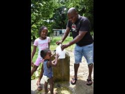 Photos by Ian Allen
Jerry Guy is accompanied by Kai Walters (centre) and Ariana Cheeke as he catches water from Marley Spring on Tuesday.