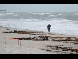 A beachgoer walks along the shore as waves churned up by Tropical Storm Isaias crash near Jaycee Beach Park on Sunday, in Vero Beach, Florida. 