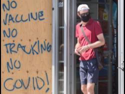 A man wears a face mask as he passes by graffiti reading ‘No vaccine, No tracking, No COVID’, in Montreal on Sunday, as the COVID-19 pandemic continues in Canada and around the world.
