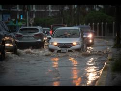 Motorists navigate through a flooded Trafalgar Road in St Andrew on Sunday.