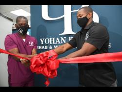 Yohan Blake, (Right) Chairman of Yohan Blake Wellness Centre and Therapist, Rupert Fearon (left), cutting the ribbon at the opening of the wellness centre official opening at 47d Old Hope Road in Kingston yesterday.