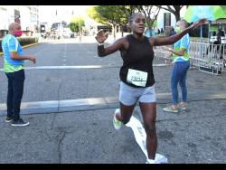 Credit: Rudolph Brown Jozanne Harris runs through the tape to win the women’s invitational at the Sagicor SIGMA Corporate 5K race in New Kingston yesterday as Mark Chisholm, Executive Vice President, Sagicor Life Jamaica, Individual Life Division and Cathy Allen, Chief Actuary of Sagicor Group Jamaica look on.