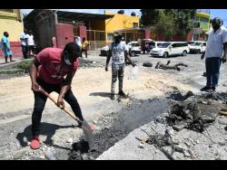 Owen Thomas (left), taxi operator, does his part to fix the roadway.