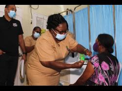 Monica Watson (right) receives her first dose of the COVID-19 vaccine from Olufunke Adetola, senior public health nurse, at the Summerfield Community Centre in Clarendon. Looking on is Dr Christopher Tufton, minister of health and wellness.