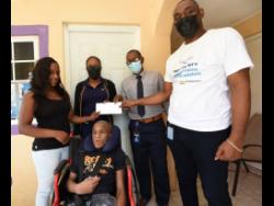 Jodeon Davis-Lawrence (left) accepts a Christmas gift from Lloyd Richardson of the NCB Foundation at a Wish Upon The STAR promotion at her home in Heartease, Manchester. Sharing the moment are Davis-Lawrence’s son Nickardo King (in the wheelchair), Tracy-Ann James, and Desmond Reid, also of NCB.   ,