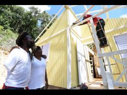 Carlton Francis (left) and Petrolina Blair look on as workmen construct their new house which is being built by Food For the Poor and Boom Energy drink.  