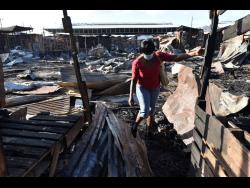 A woman walks through the rubble in a section of the Ray Ray Market that was destroyed by fire on Tuesday night.