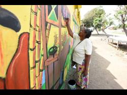Charmaine Forbes helps to create a masterpiece on a wall at the entrance to the Rae Town Fishing Village.