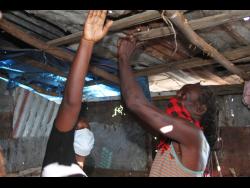 In this 2021 photo, Natoya Anderson and her spouse Jerald Dunkley point to the many holes in the roof of their kitchen.