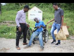 Devon Reid (centre) excitedly shows off his new wheelchair, fresh out the box. Looking on are Pastor Tilden Falconer (left) and Clement Alves.