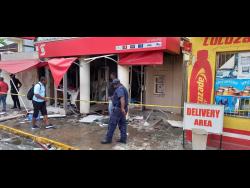 Police personnel and civilians look at the damage caused by the explosion at the Scotiabank ATM in Port Antonio, Portland last Saturday.