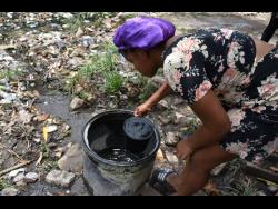Nadia Williams uses a small bucket to fetch water from the ‘well’ in Majesty Gardens, St Andrew. 