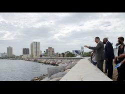 Prime Minister Andrew Holness (left) waves to a fisherman out at sea at the official handover ceremony for the Port Royal Revetment Project adjacent to the Breezy Castle Sports Complex on Wednesday in downtown Kingston. Looking on are Dr Wayne Henry, chairman of the Jamaica Social Investment Fund, and Imani Duncan-Price, who represented the Opposition Leader.