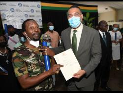 Prime Minister Andrew Holness (right) presents a land title to Zachariah Oakley during the National Land Agency’s systemic land registration and land titling ceremony at the Old Harbour New Testament Church of God in St Catherine on Wednesday.