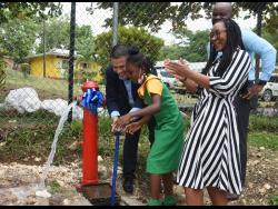 An elated Tova Hamilton (right), member of parliament for Trelawny North, claps as Matthew Samuda, minister without portfolio in the Ministry of Economic Growth and Job Creation, and Kiara Mullings, a student of Brampton Primary School, turns on a water hydrant during the official commissioning of the Baron Hill to Samuel Prospect Pipeline Replacement Project in Trelawny on Thursday.
