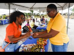 Shellyann Tracey (left), the owner of Nature’s Queen Blended Seasonings, explains how she prepares her hand-made seasoning to Shurnette Bailey Byfield at the Social Development Commmission fair on July 1 in St Catherine.