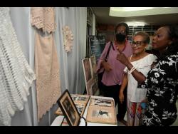 From left: Cara Lewis, Ruth Ho Shing and Angela Jarrett check out pieces done by the late Leonie Forbes during a tribute concert at the Little Theatre on Monday. 