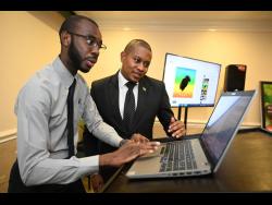 Mario Reynolds (left), research officer, genealogy unit, Registrar General’s Department (RGD) demonstrates the Family Tree Maker to Minister without Portfolio in the Office of the Prime Minister Floyd Green at the RGD launch of online products and services at the Courtleigh Hotel and Suites on Wednesday.