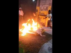 Screenshot shows Sizzla (right) and another man watching the fire as it burns the Billboard plaques. 