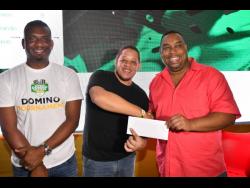 Gavin Simpson (centre) collects his winner’s cash prize from Kevin Peart of Kingston Jerk Centre, with Dwayne Tulloch, senior vice-president of retail and operations at Supreme Ventures, sharing in the celebration. Simpson won $150,000 for capturing the pilot Supreme Masters Domino Tournament at Kingston Jerk Centre on Sunday.