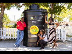 Senior staff members of Bridgeport High School, (from left) Malcolm Nelson, Paula Taylor, and Marcia Palmer, pose in front of one of the two 1,000-gallon water tanks presented to the school by Bigga last Friday.