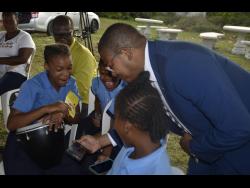 Minister without Portfolio in the Office of the Prime Minister, Floyd Green (right), shows students from the Mountainside Primary School in St Elizabeth how to access free Wi-Fi service in the community, at the commissioning ceremony by the Universal Service Fund (USF), on Wednesday.