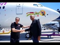 CEO of Caribbean Airlines, Garvin Medera (right), shakes hands with Reggae Sumfest promoter Joe Bogdanovich, on the revealing of the Reggae Sumfest decal, which stands out on the side of this Caribbean Airlines aircraft. 