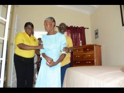 Minister of Local Government and Rural Development, Desmond McKenzie, and CEO of the Westmoreland Municipal Corporation, Marvalyn Pitter (left), assist Joyce Booth as she tours her new home.