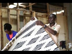 Manager of TEXFAD John Baptist Okello checks a handmade carpet woven from banana fiber threads at the factory in Sonde, Mukono district, Uganda. 