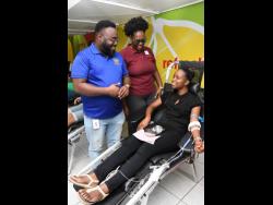Jamar Howell (centre), chairman of the JN Sports and Social Club, and Toni Moy Stewart (centre), immediate past president of the Rotaract Club of Kingston (RCOK), speak with rotaractor, Shari Watson, as she prepares to donate blood at the 2022 staging of the RCOK’s Christmas Blood Drive, held at the JN Bank Chief Office in Half-Way Tree, St Andrew.