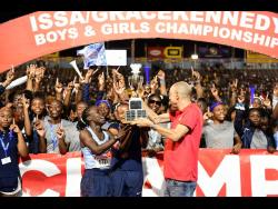 Edwin Allen High's co-captains Tonyan Beckford (left) and Monique Stewart receive the girls' champs trophy from Chief Executive Officer of GraceKennedy at the ISSA/GraceKennedy Boys and Girls' Athletics Championships at the National Stadium tonight.