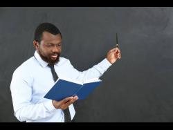  A teacher pointing at blackboard in classroom.