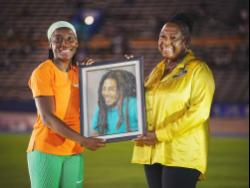 Minister of Culture, Gender, Entertainment and Sport, Olivia Grange (right), presenting Marie Talou Smith (left) with a Bob Marley painting, her award for first place in the women’s 100m at the Jamaica Athletics Invitational held at the National Stadium on Saturday, May 11, 2024. Sports Minister Grange says work on resurfacing the track at the National Stadium is progressing on schedule.