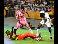Credit: Photos by Gladstone Taylor/Multimedia Photo Editor Cavalier Soccer Club’s goalkeeper Vino Barclett (on ground) uses his foot to block the ball as his teammate Jeovanni Laing (right) defends against Sergio Busquets of Inter Miami during their Concacaf Champions Cup quarter-final football match at the National Stadium in Kingston on Thursday, March 13.