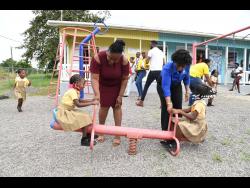 Claudine Allen (right), general manager of the JN Foundation, and Monica Henry-Grandison, principal of Jefferey Town Basic School, assist students on the play equipment during an official handover of a play area to the school.