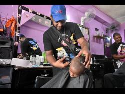 Barber Alex Smith puts the finishing touches on a fresh trim for a student at Netty’s Beauty and Barber Salon on East Queen Street, downtown Kingston, last Friday.