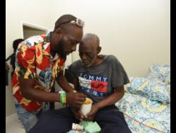 Credit: Ian Allen Ronald Reddie (right) is assisted by his son, Omar, as he drinks soup in the comfort of their new house in Gayle, St Mary.