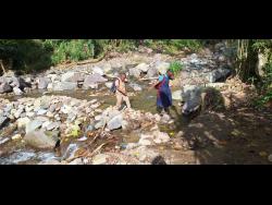 Anderson twins make their way across the river, part of their daily commute after Hurricane Melissa caused serious damage to the road network in East Rural St Andrew.