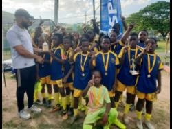 Balmagie Primary School captain, leading scorer and the competition’s MVP, Kevin Grant receives the Insports St Andrew Primary Schools Football trophy from Insports officer Sylvester Campbell (left) following the final against St. Richards Primary at UWI Bowl, Mona on Friday. Balmagie won 4-3 on penalties after playing to a 0-0 draw.