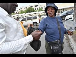 A customer collects his bag from Simone ‘Shelly’ Henry, who keeps phones and bags safe outside the US Embassy in Kingston.